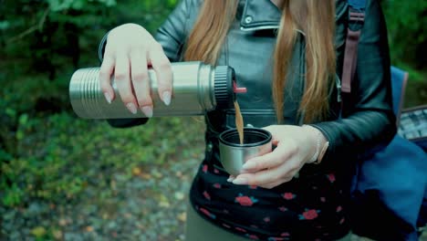 enjoying tea in the woods, women in the forest takes break and pour tea for herself