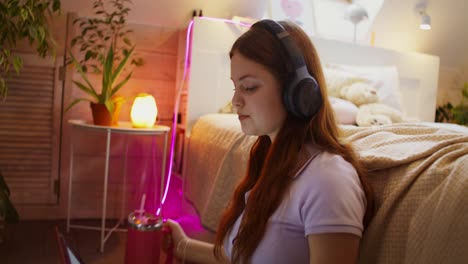 teenage girl relaxing in her bedroom with headphones and a drink