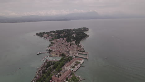 Toma-De-Drone-De-Simione-Italia-Mirando-La-Antigua-Fortaleza-En-Un-Día-Gris-Con-Barcos-En-El-Agua-Cerca-Del-Lago