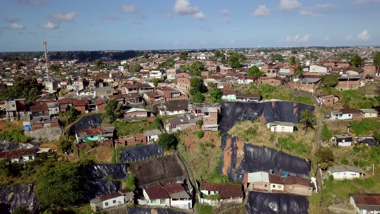 Daylight aerial shot above Macaxeira neighborhood in Recife Brazil revealing hillside communitys simple houses vehicles and makeshift tarps illustrating poverty risk and social inequality urban zone