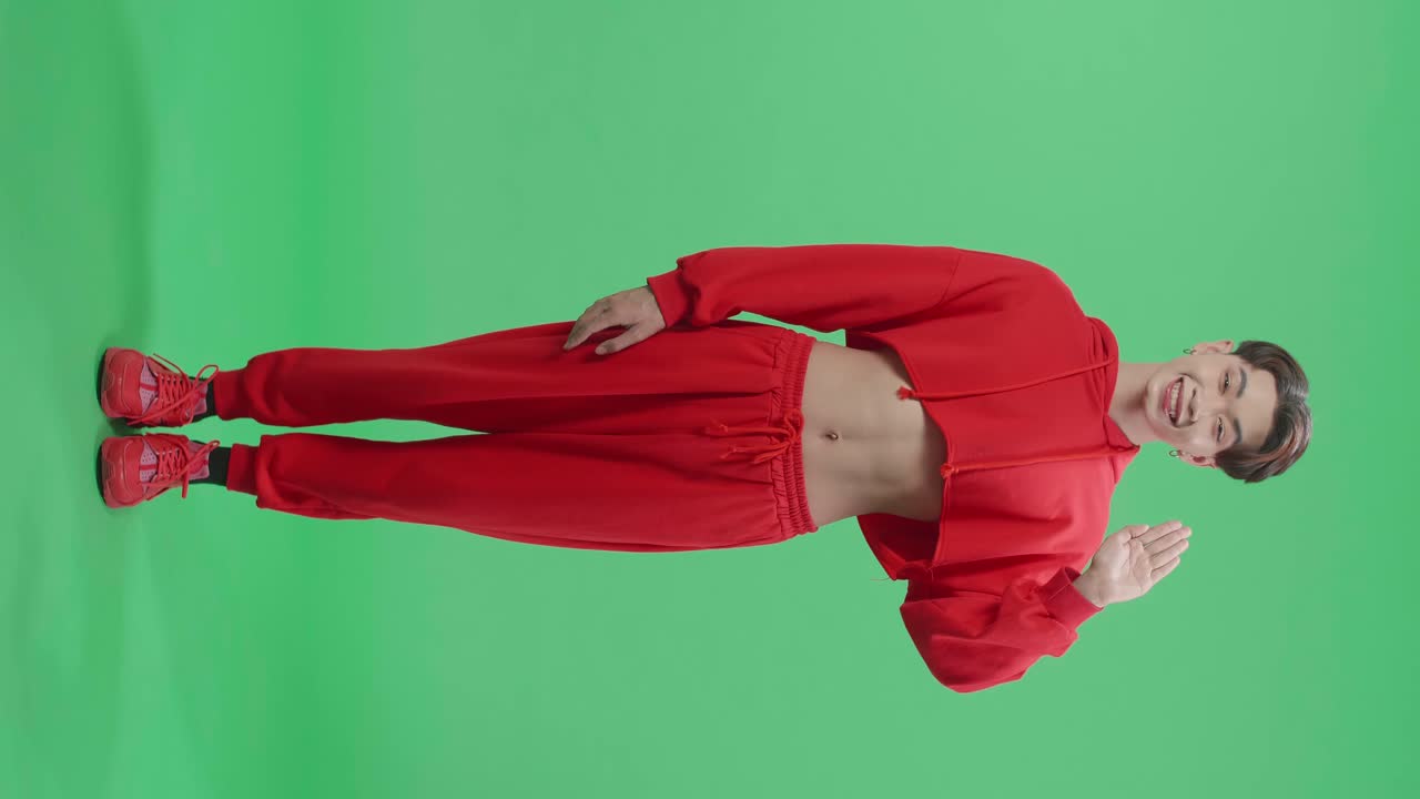 Full Body Of A Smiling Asian Transgender Male Waving Hand And Say Hi While Standing On Green Screen In The Studio