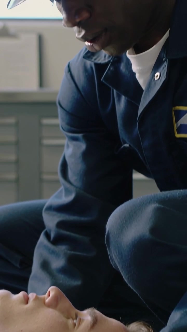 Video verticale: Tiene un dispositivo tecnologico in uniforme blu scuro, controllando le vie respiratorie di un uomo dopo una caduta, con un elmetto da lavoro.