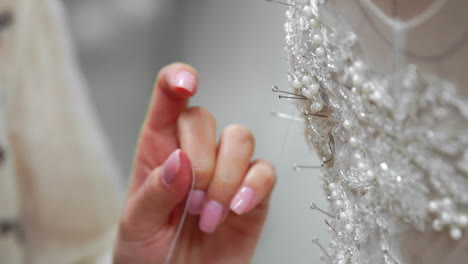 Close-up-fashion-designer-for-brides-in-his-Studio-pins-needles-lace-wedding-dress.-Seamstress-creates-an-exclusive-wedding-dress.-Secure-with-pins-and-needles-outline.-Small-private-business.-Sew-rhinestones-and-crystals-to-the-dress-thread-and-needle.-Jewelry-work.