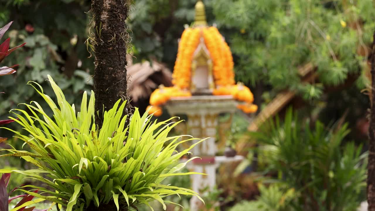 una escena tranquila de jardín con exuberante vegetación y un santuario tradicional tailandés adornado con guirnaldas de mármol
