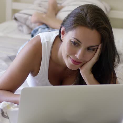 young woman laying down in bed using laptop