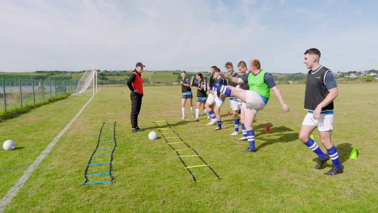 Male and female soccer players warming up and moving their legs with coach on pitch