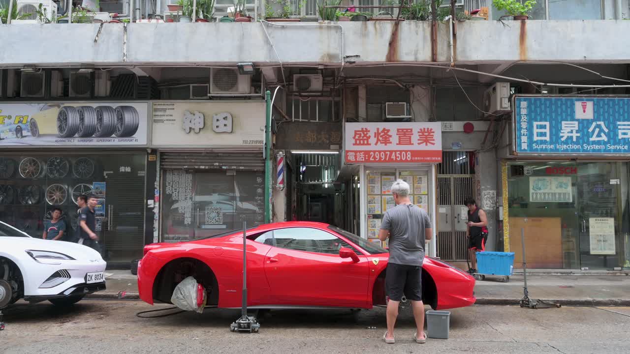 A juxtaposition scene in a low-income district of Hong Kong, China, where a mechanic repairs a red Ferrari 458 Italia on the street.
