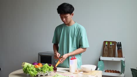 asian young man peeling fresh carrot, ingredients for making salad at home