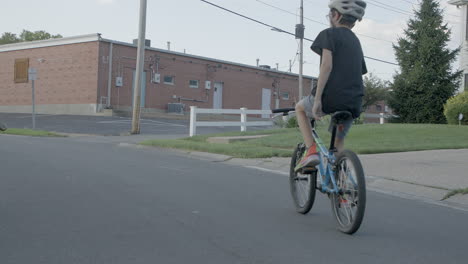 a kid rides his bike up the street in the suburbs on a summer day in slow motion