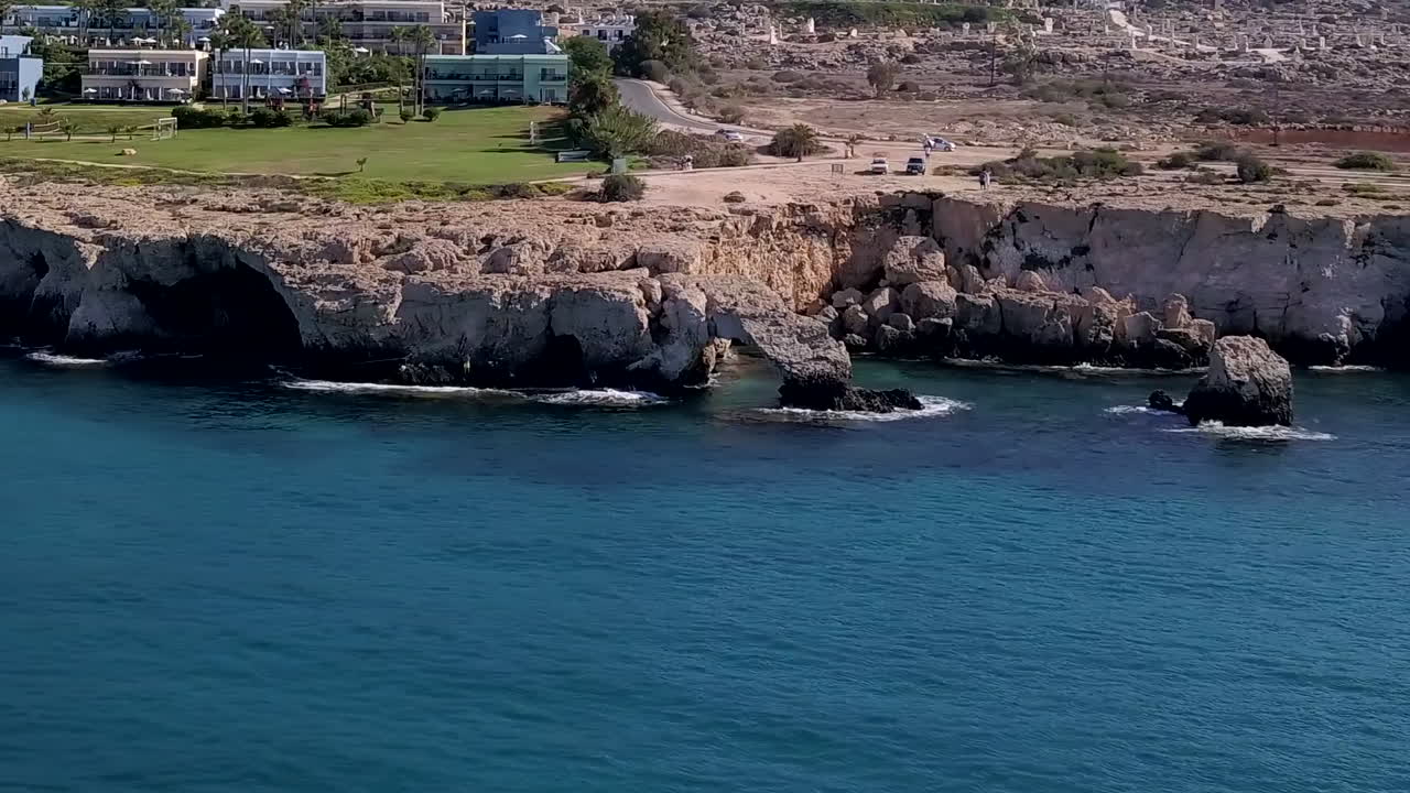 Aerial drone shot of a rocky sea coast with a tourist resort in the background