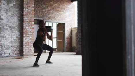 shirtless african american man exercising with medicine ball in an empty urban building