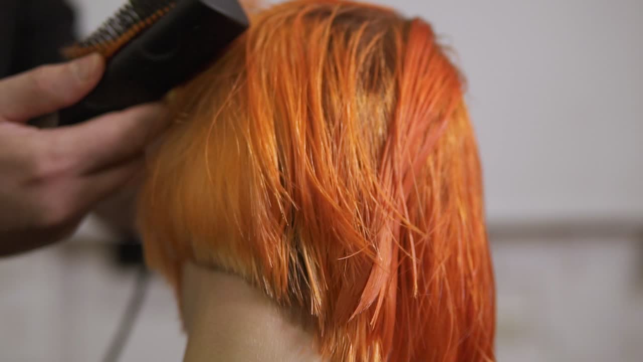 머리카락을 잘라낸 후 헤어 드라이어를 사용하는 전문 헤어드라이어의 가까운 모습. 미용실에서 젊은  ⁇ 은 머리 여성. 느린 움직임 촬영