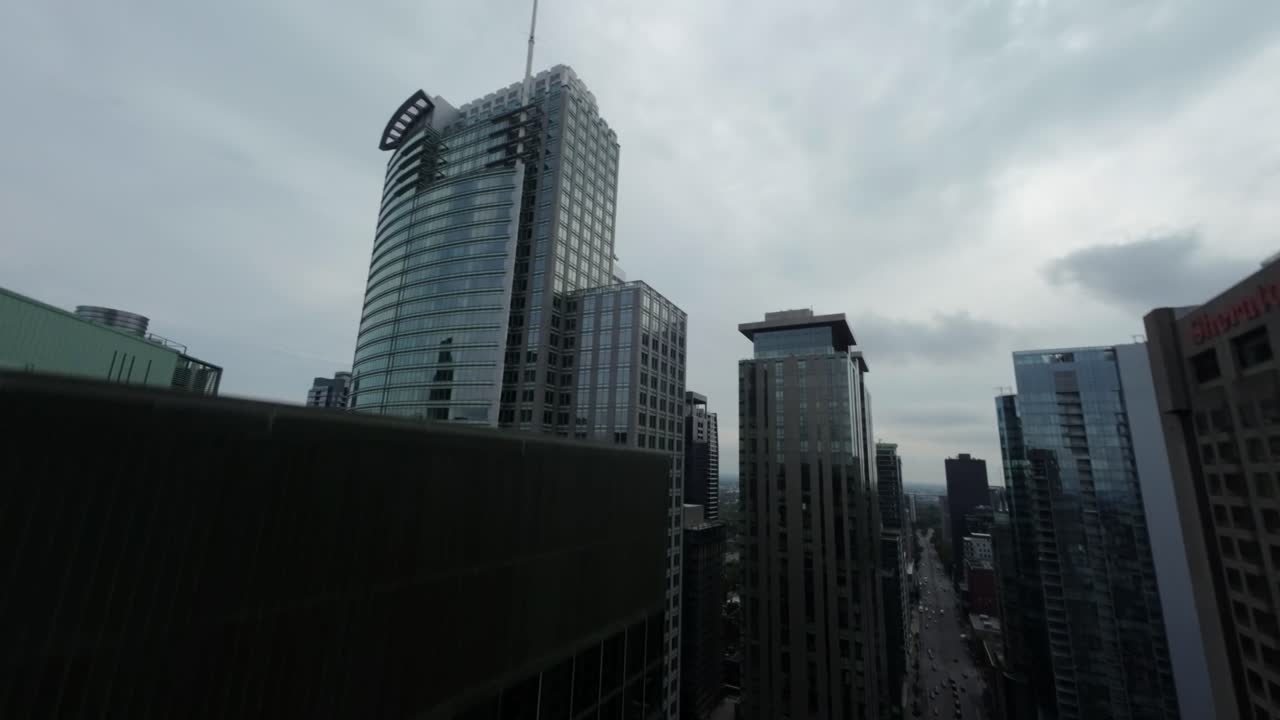 FPV drone flies dynamically along street flanked by tall buildings, then ascends high for stunning aerial view of downtown Montreal at Square Dorchester.