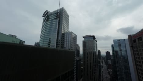 fpv drone flies dynamically along street flanked by tall buildings, then ascends high for stunning aerial view of downtown montreal at square dorchester.