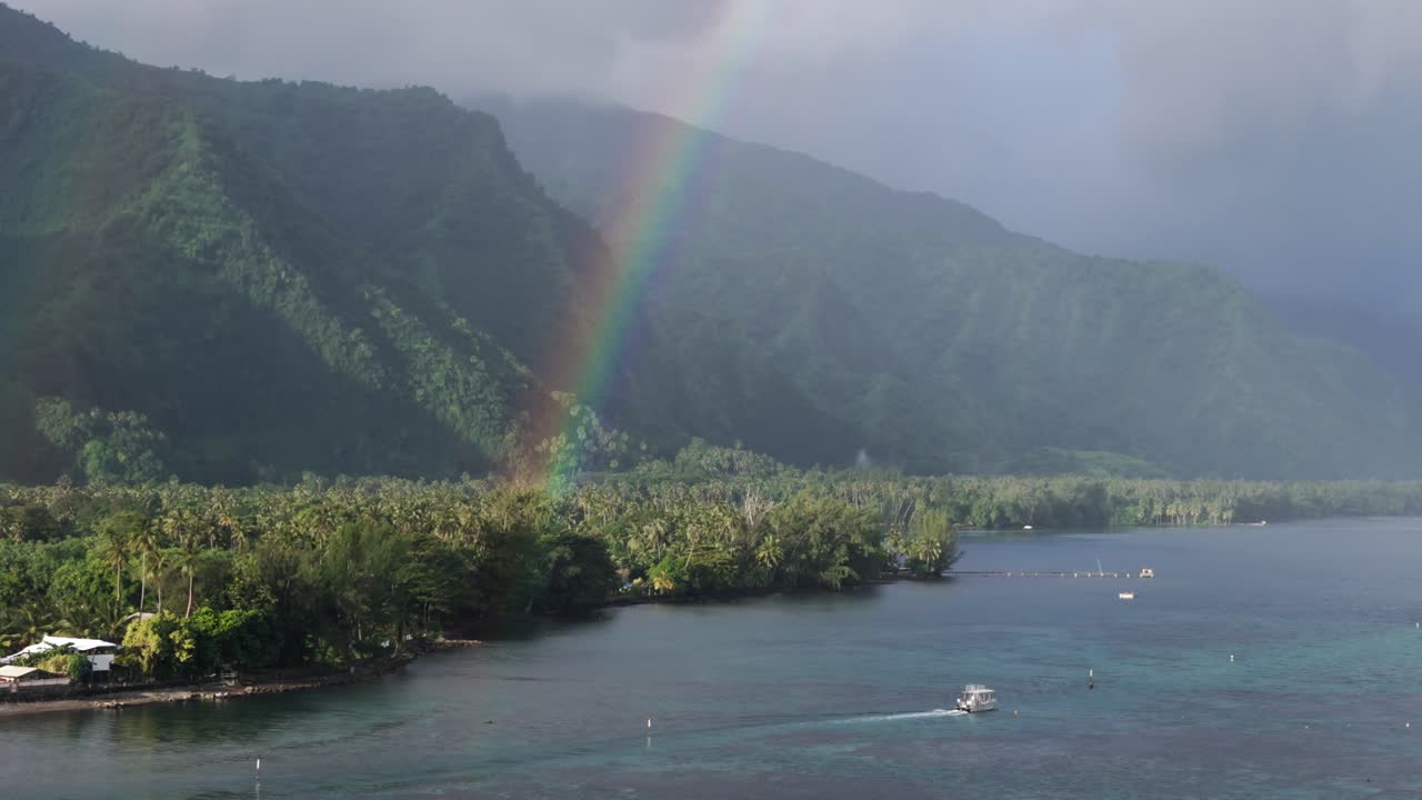 Boat Sailing Along The Teahupoʻo Village With Rainbow And Green Palm Trees In Tahiti, French Polynesia, France. - aerial shot