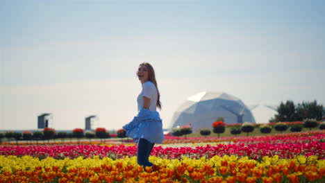 vista trasera de una chica riendo corriendo por un campo de tulipanes con un edificio futurista.