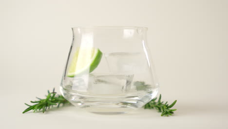 Glass-is-filled-with-cold-ice-and-green-fresh-lime-slices-adorned-with-Rosemary-on-white-background