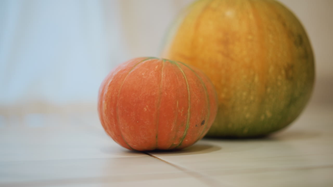 Small pumpkin on kitchen floor bathed in soft morning light, green pumpkin blurred in background, beige tile surface and warm rustic mood, cozy home kitchen produce ready for cook prep