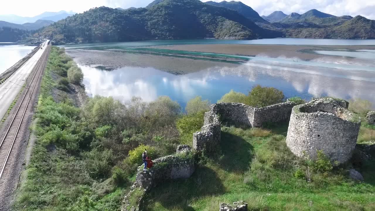 vista aérea de una pareja romántica en las ruinas de un castillo histórico junto al lago