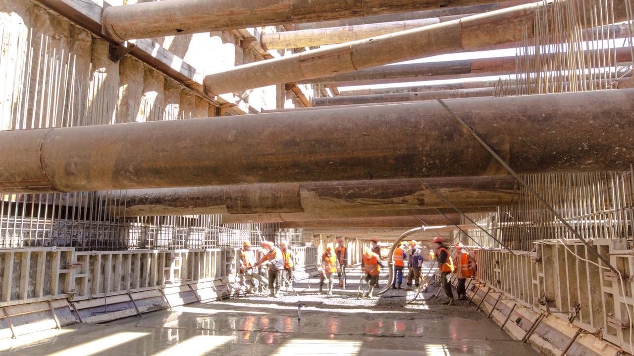 Workers pouring concrete in large huge ditch pit tunnel timelapse. Reinforcing structures from thick iron pipes of beams and structures at the construction site of the underground metro station line