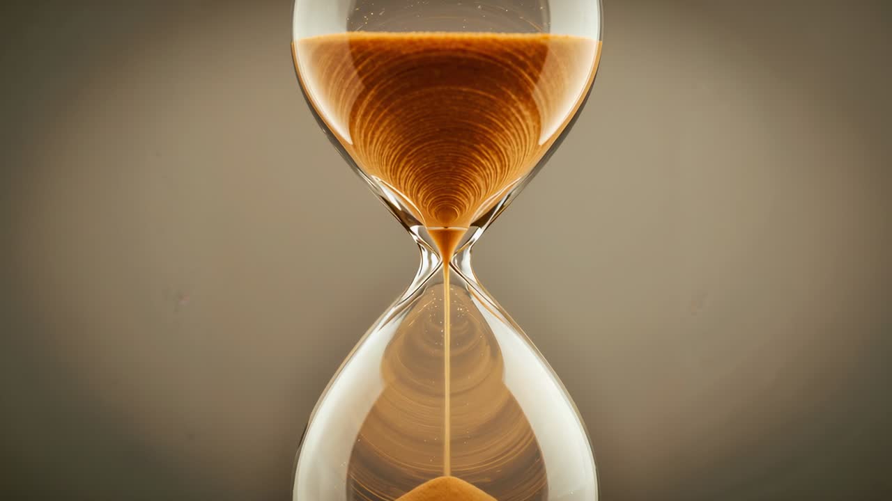 Slipping fine amber sand through clear glass hourglass under gravity in studio, measuring time