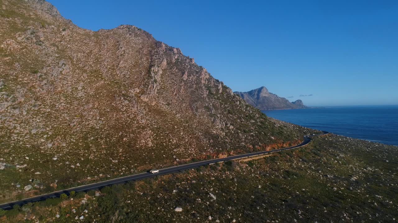 여름날 바다 쪽 산길에서 운전하는 랜드 로버의 공중 추적 샷