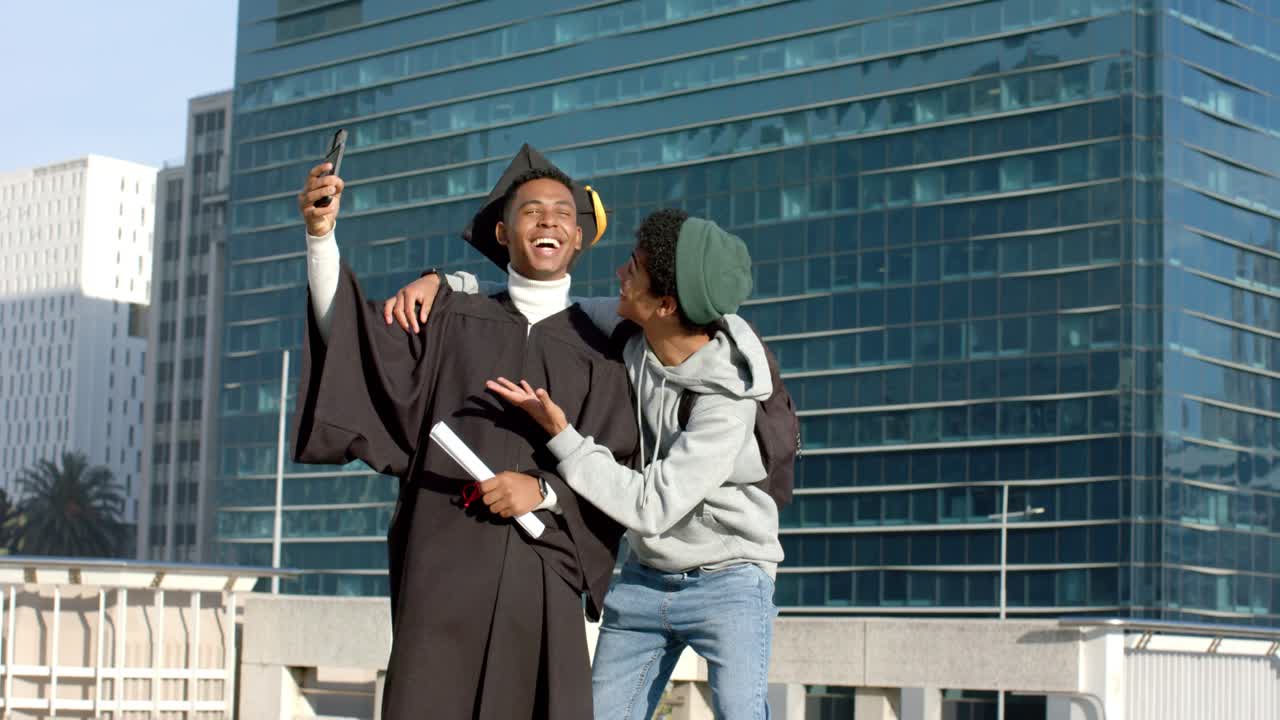 Male friends stepping onto rooftop raising smartphone capturing graduation selfie with diploma