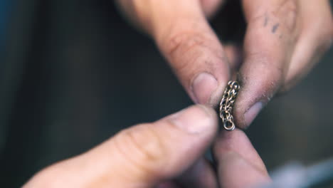 jeweler connects link and looks at chain in workshop closeup