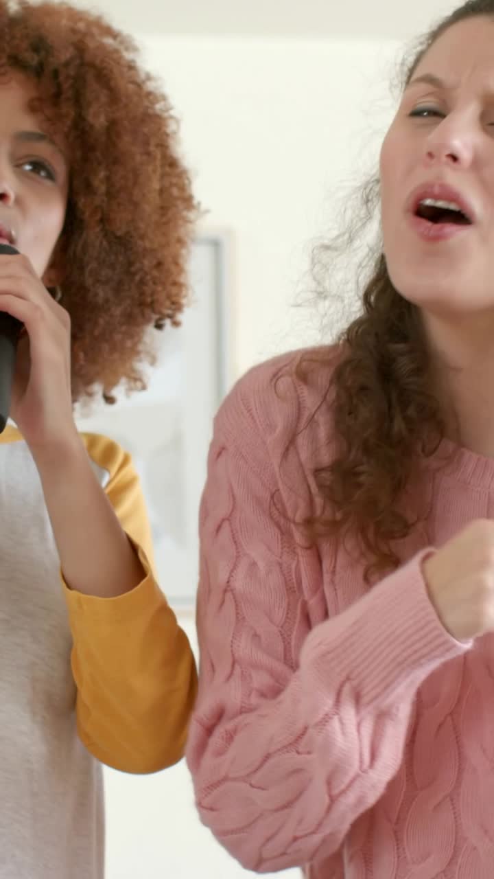 Video vertical: Dos mujeres cantando a dúo en casa por diversión con un micrófono mientras comienza una canción; una de ellas lleva un suéter rosa.