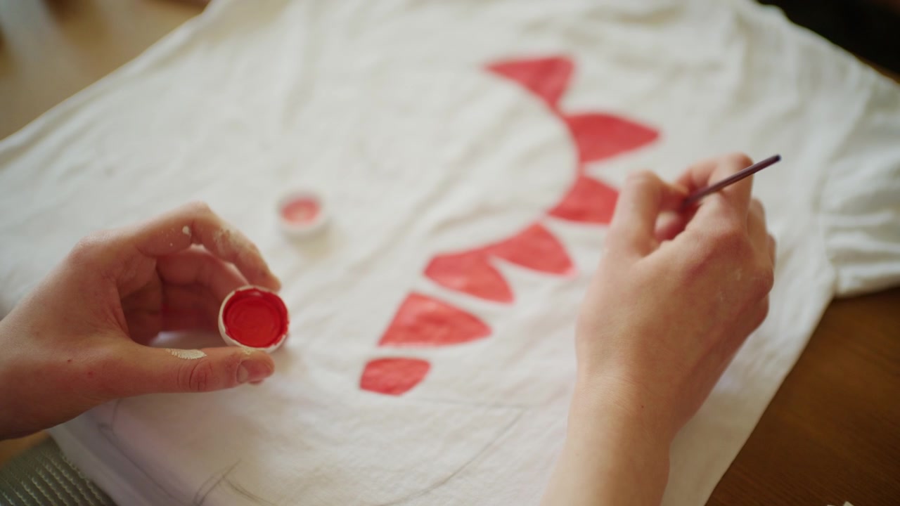 Close up of an artist painting red decorative shapes onto a white T-shirt using fabric paint
