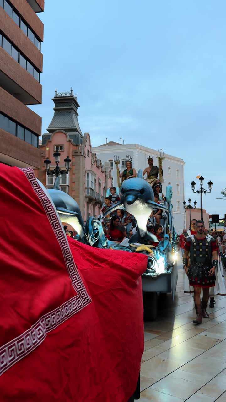 Alicante, İspanya, 6 Ağustos 2025: Kamyon üzerinde Roma figürleri bulunan festival geçit töreni aracı. Şehirde, Roma kostümlü aktörler ve süslenmiş araç üzerinde yunus heykeli içeren halk kutlaması.