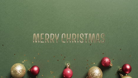 merry christmas text in gold with baubles on green background