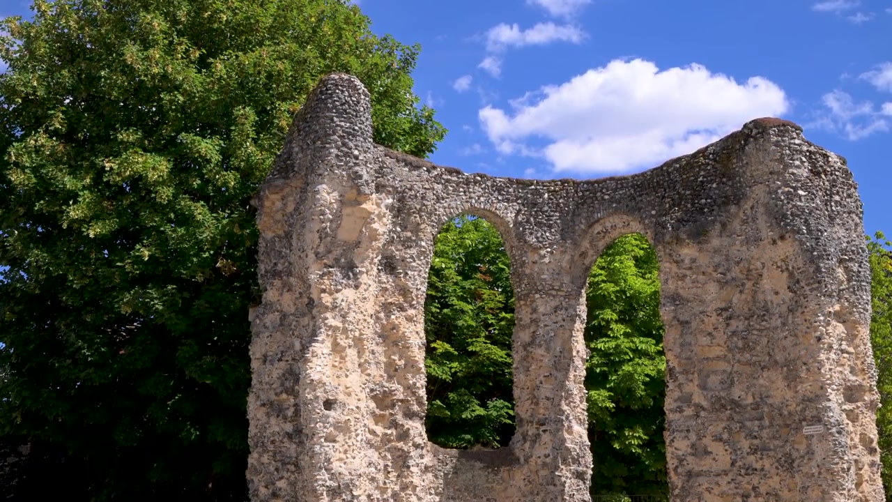 Forvitret steinbue fra ruinene av Reading Abbey innrammet av løvrike grønne trær under en lys blå sommerhimmel