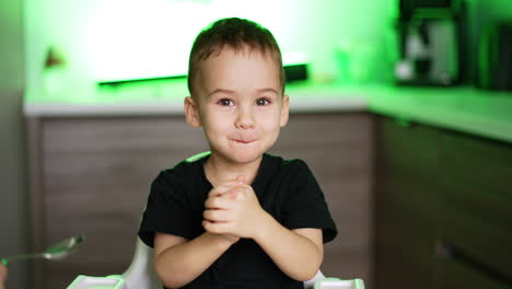 feeding a cute caucasian toddler boy from spoon. smiling child chews his food and plays with hands. blurred backdrop.