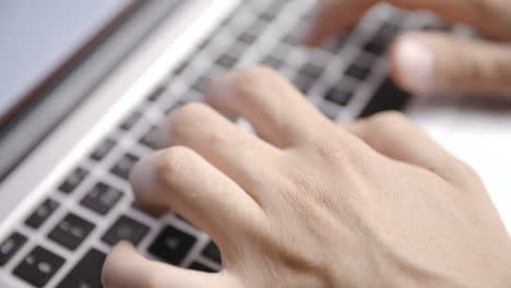 close-up from above of young male hands typing on laptop keyboard