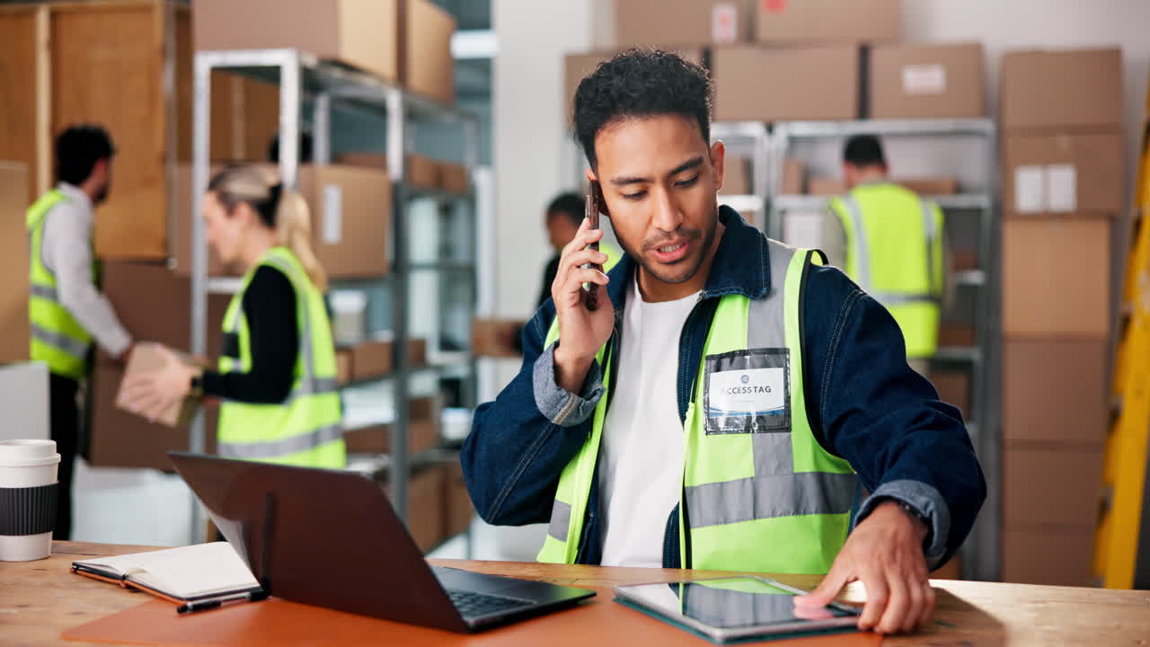 Warehouse worker on a phone call using a laptop and tablet