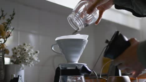 la mano getta il caffè macinato nel filtro v60 con la smerigliatrice in primo piano