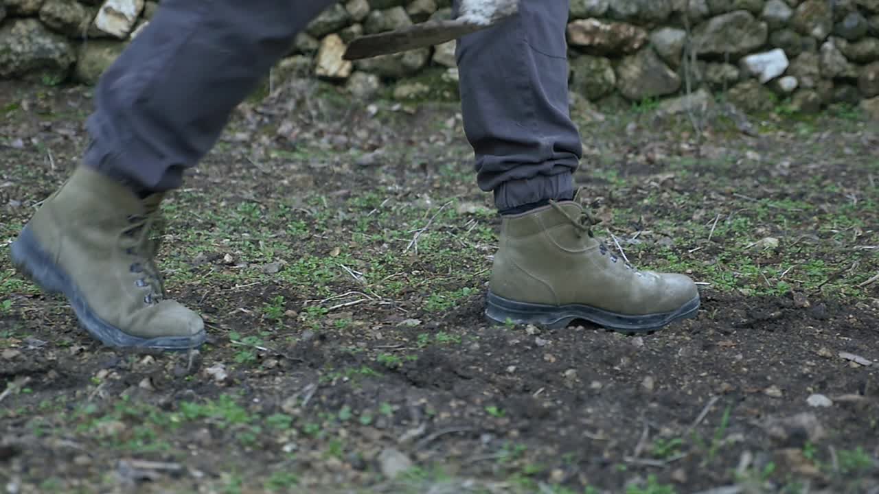 Work boots walking slowly on a damp, dark ground, ideal for representing fertile land ready for planting, fieldwork, farming, or after a beneficial rain