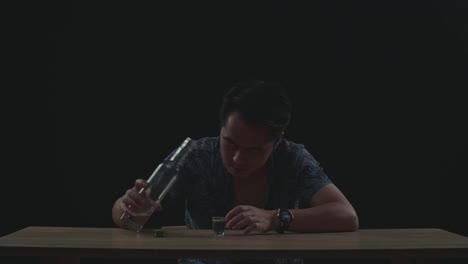 술에 취한 우울한 아시아인 남자가 검은색 배경에서 술을 마시기 전에 글라스에 보드카를 부어
