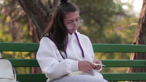 Chica-Tirando-De-Su-Cabello-Detrás-De-Su-Oreja-Mientras-Lee-Un-Libro-En-Un-Parque