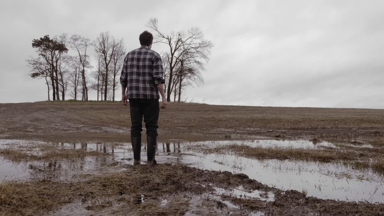 Man in wellies walking through puddles in countryside, graded slow motion
