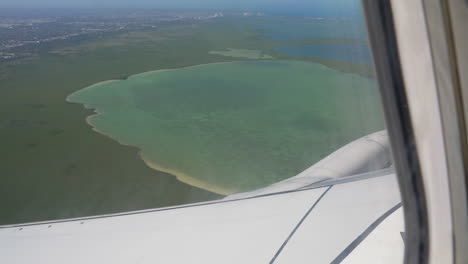 airplane flying over turquoise blue water lagoon as seen from passenger window.