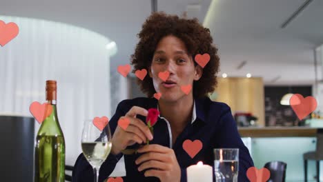 Animation-of-hearts-over-biracial-man-drinking-wine-and-having-video-call