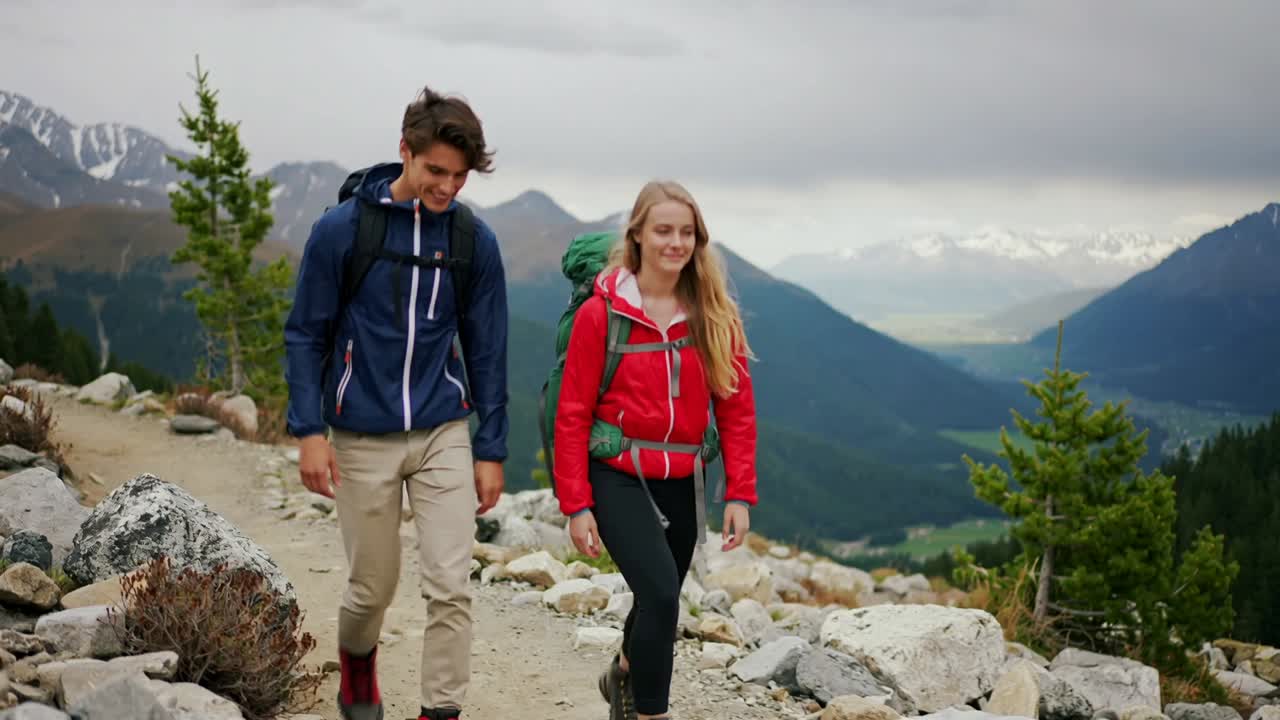 Escursionisti che camminano con giacche rosse e blu navy e zaini che seguono un sentiero alpino con vista sulla valle