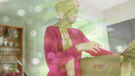 biracial woman in hijab taking vegetables out of box in kitchen over spots of light