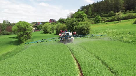 Tractor-driven-through-a-lush-green-field-spraying-chemicals-as-it-goes