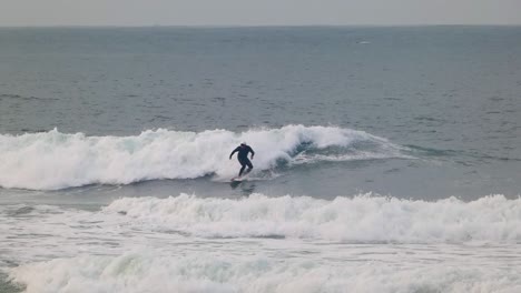 Surfer-skims-down-the-front-of-the-wave-trying-to-escape-the-wall-of-water-behind-him-in-moody,-cold-water-light-light