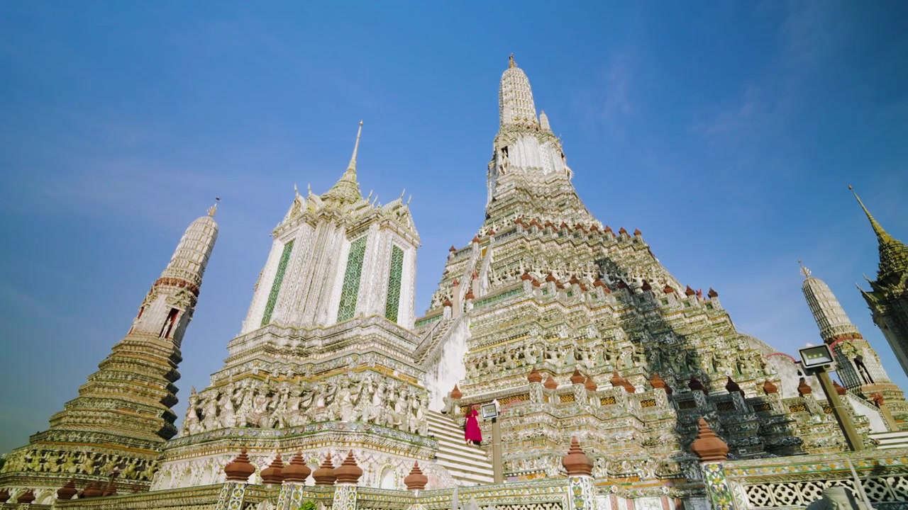 Donna in abito rosso presso l'iconico Prang Centrale (Guglia) al Wat Arun, Tempio dell'Alba a Bangkok, Thailandia. Scatto dal basso