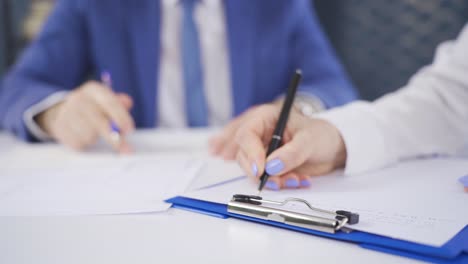 close-up hands of woman taking notes and male employee reviewing project.