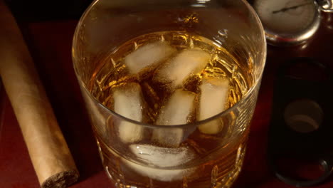 vaso de whisky en las rocas con cigarro, cortador de cigarros y reloj de bolsillo antiguo